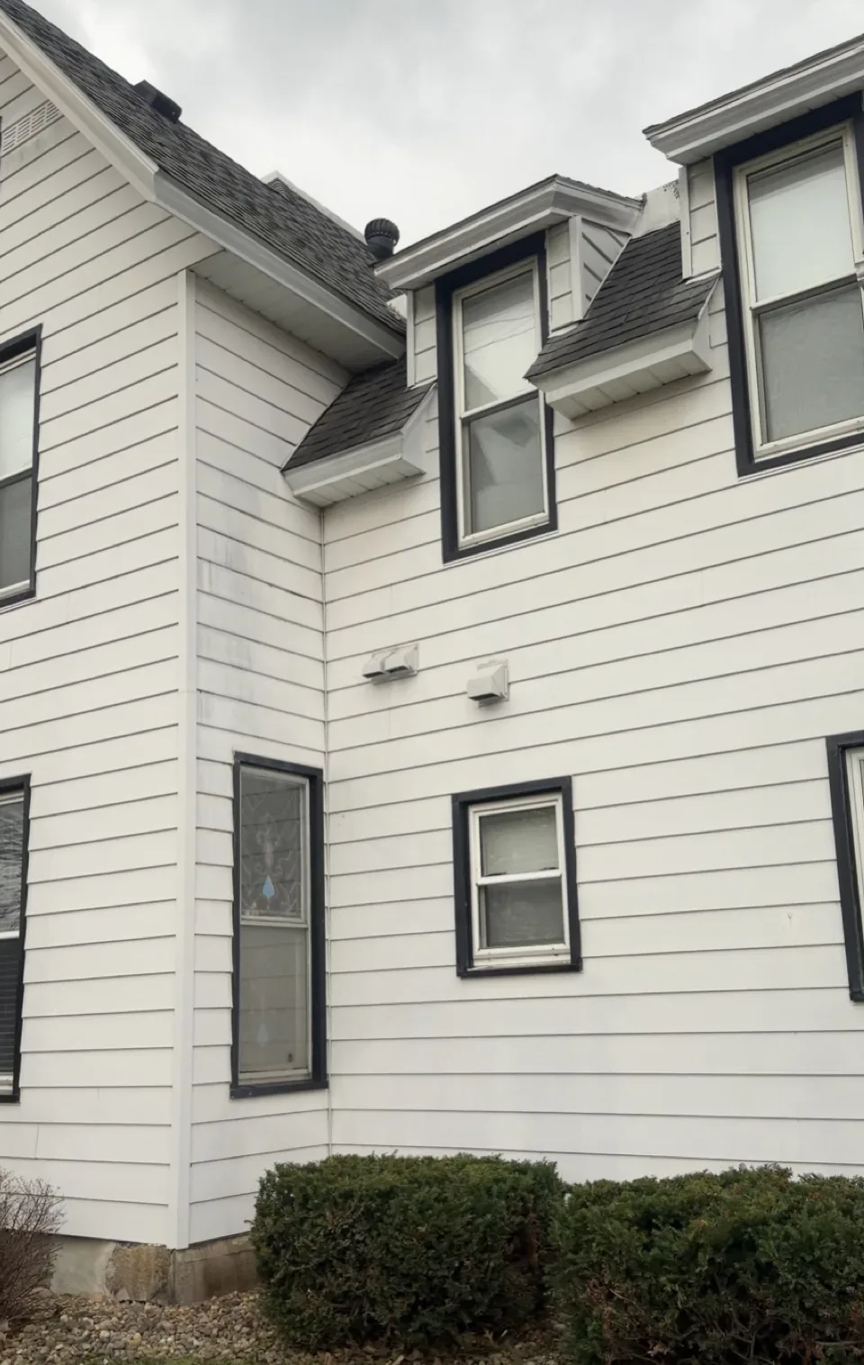Two-story white siding home, green algae on the north wall, after