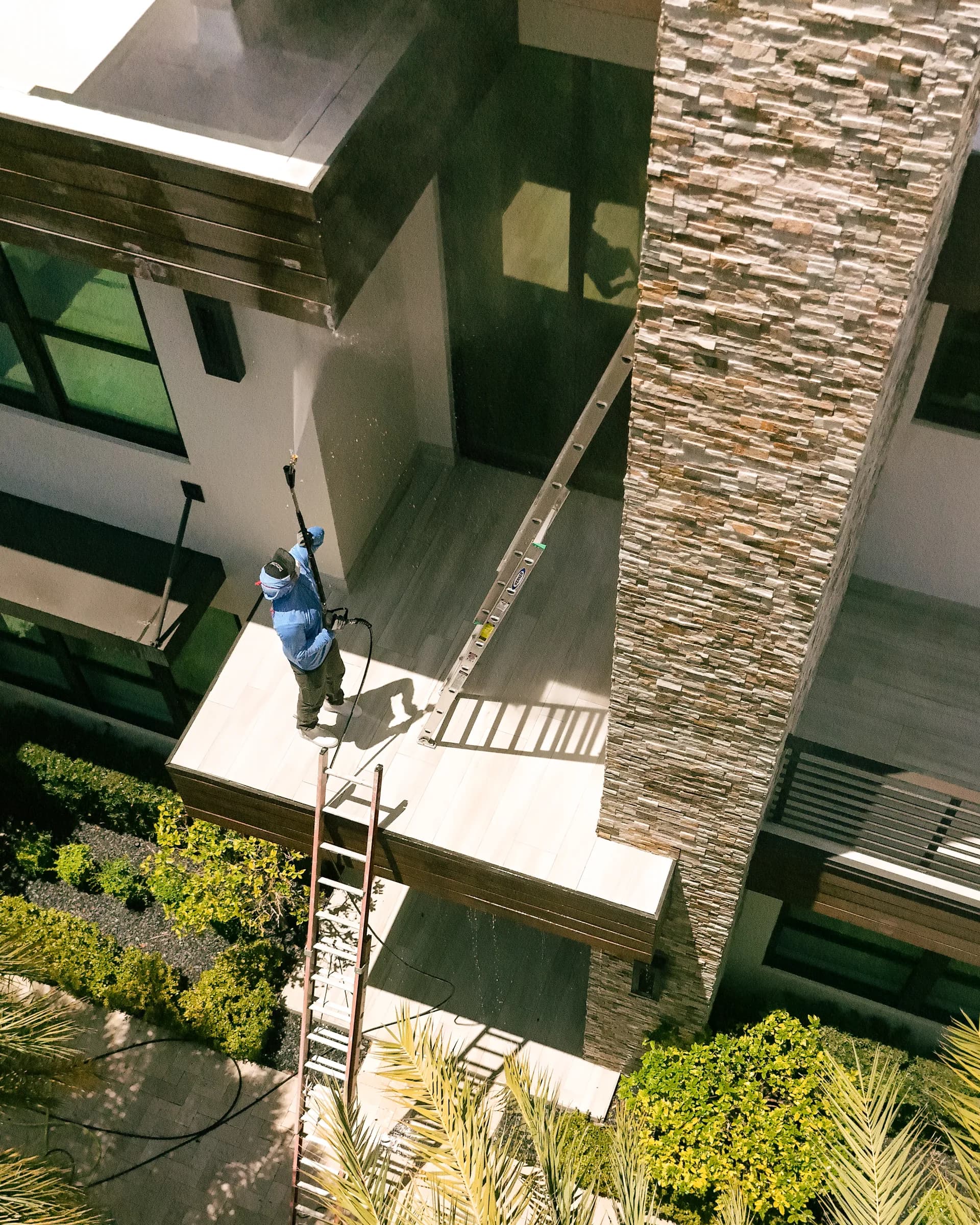 Crew on a ladder soft washing a two-story modern home