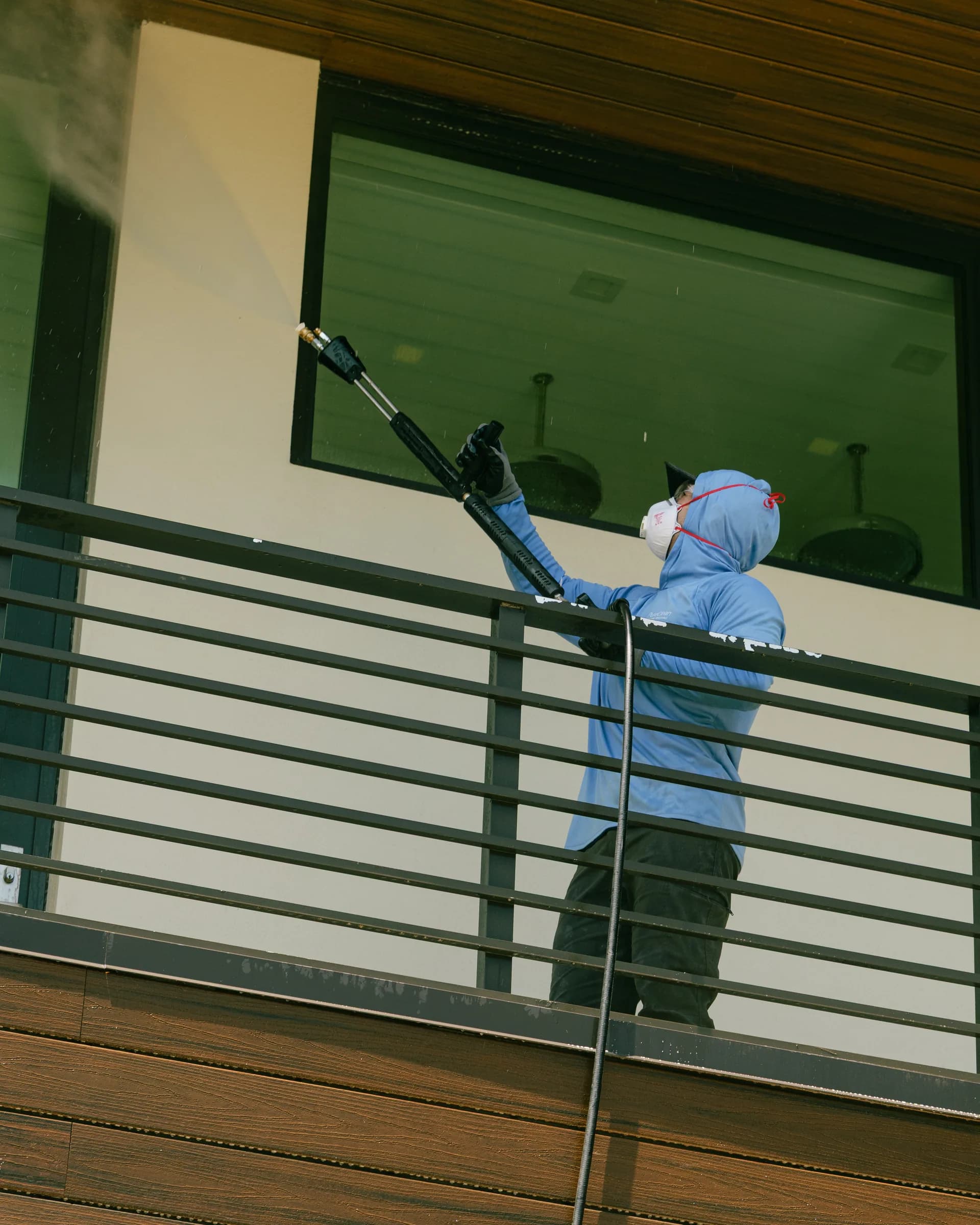 Crew member cleaning second-story glass from a balcony